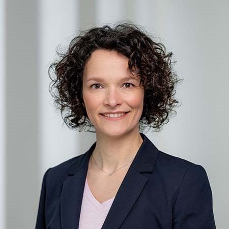 Eine Person in einem dunklen Blazer und einem hellen Oberteil.